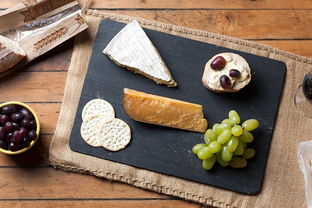 Käsebrett mit Brie, Weintrauben und Crackern neben einem Glas Rotwein auf einem Holztisch