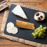 Käsebrett mit Brie, Weintrauben und Crackern neben einem Glas Rotwein auf einem Holztisch
