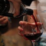 Rotwein wird aus einer Flasche in ein Glas gegossen, das eine Hand hält