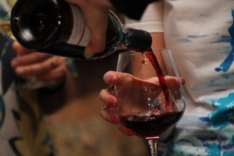 Rotwein wird aus einer Flasche in ein Glas gegossen, das eine Hand hält