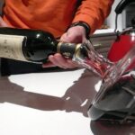 Rotwein wird aus der Flasche in einen schräg gehaltenen Kristalldekanter gegossen