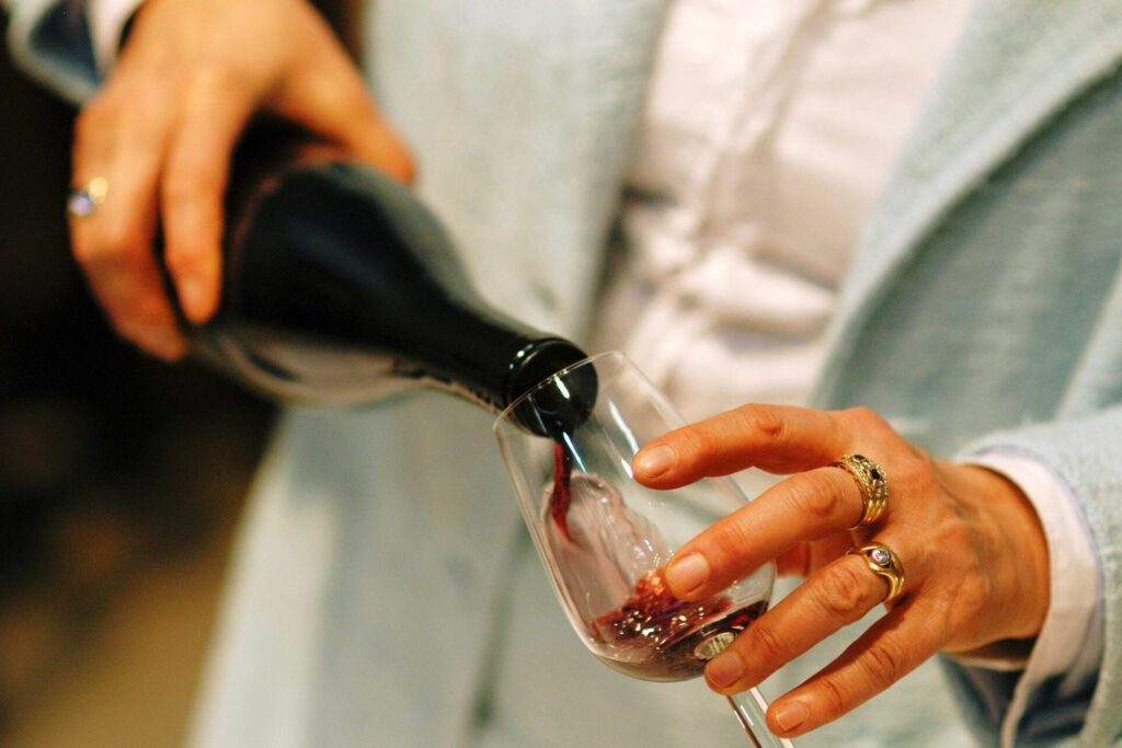 Frau schenkt Rotwein aus einer Flasche in ein Glas ein