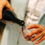 Frau schenkt Rotwein aus einer Flasche in ein Glas ein