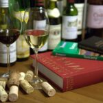Weinbücher, Korken und zwei Weingläser mit Rot- und Weißwein vor mehreren Weinflaschen
