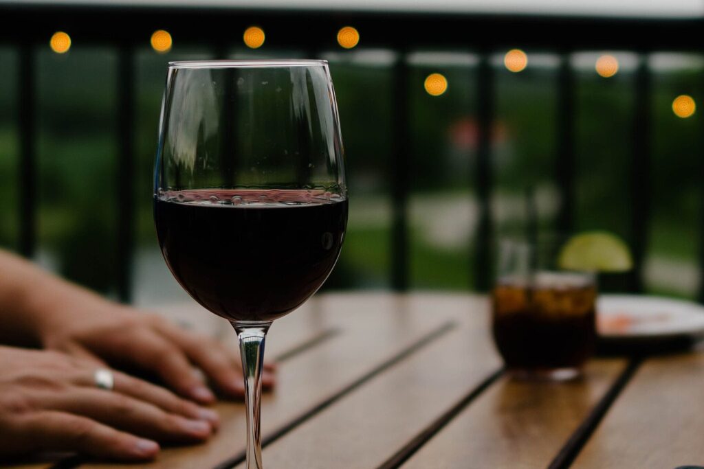 Glas Rotwein auf einem Holztisch im Freien, im Hintergrund unscharfe Lichter