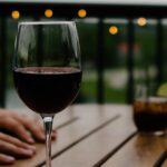 Glas Rotwein auf einem Holztisch im Freien, im Hintergrund unscharfe Lichter