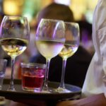 Kellner trägt ein Tablett mit Weißweingläsern und einem Glas Roséwein
